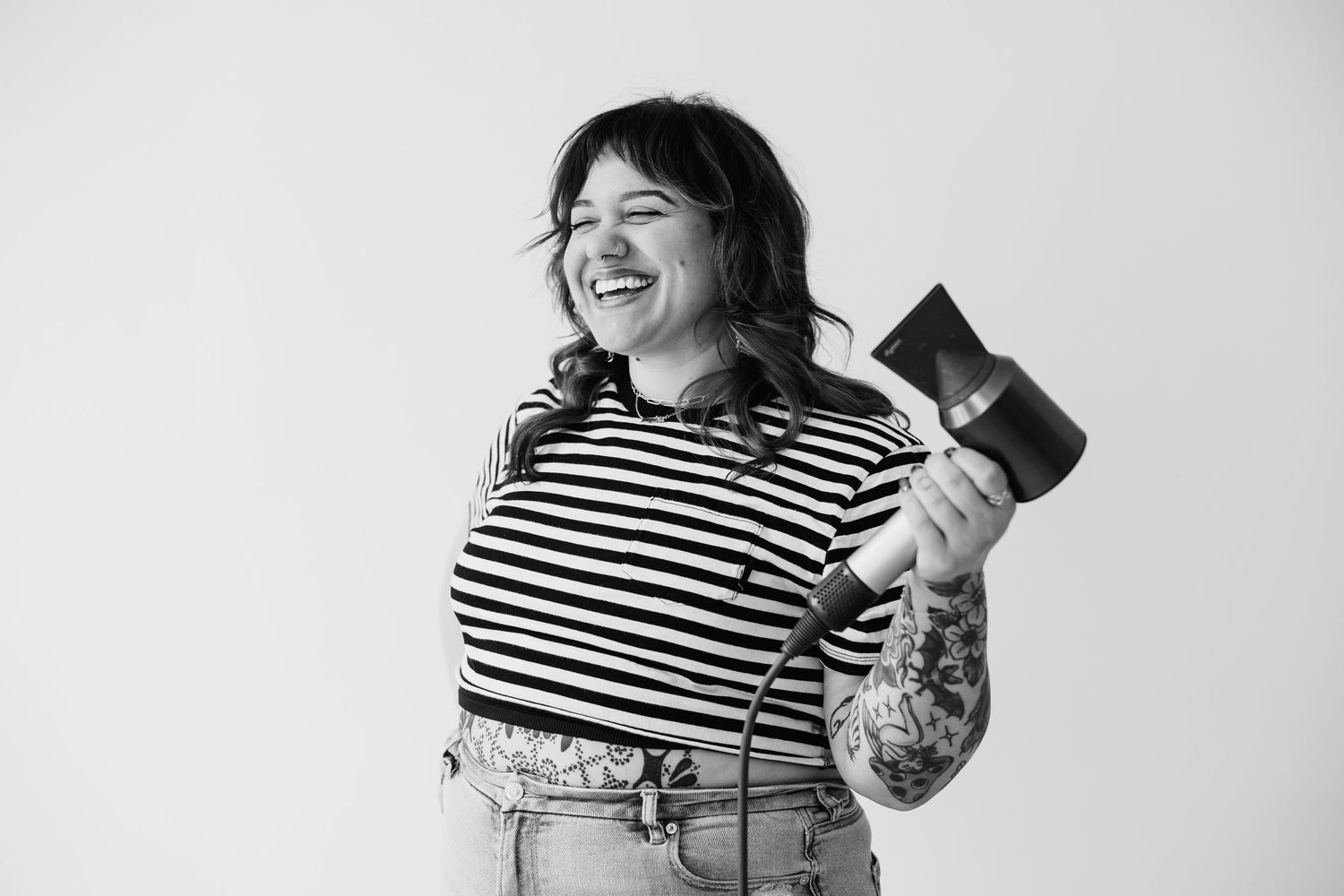 Laughing tattooed woman in striped shirt holding camera in black and white portrait.