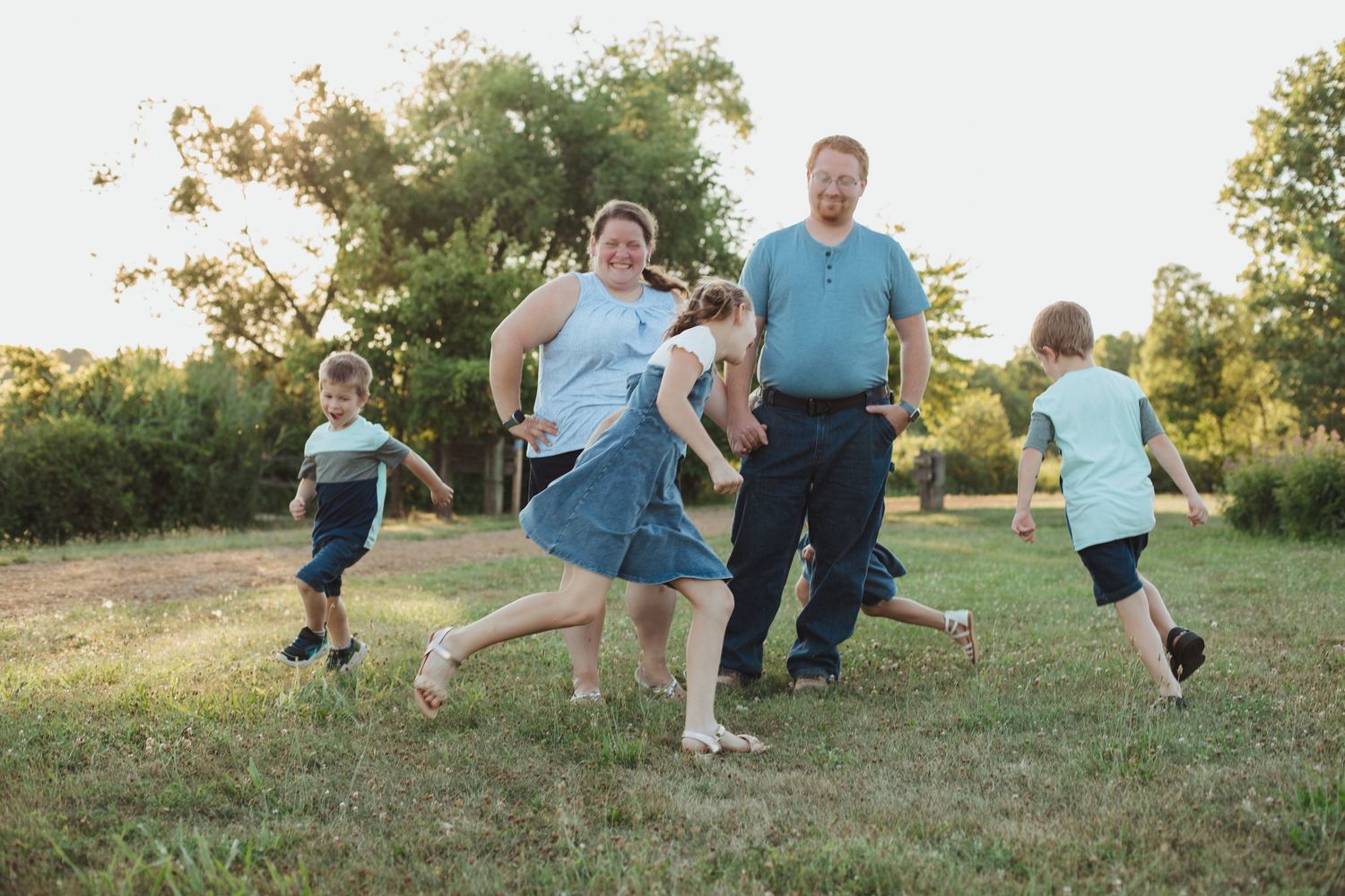 Family playing outdoors in green field at golden hour with parents and children running joyfully.