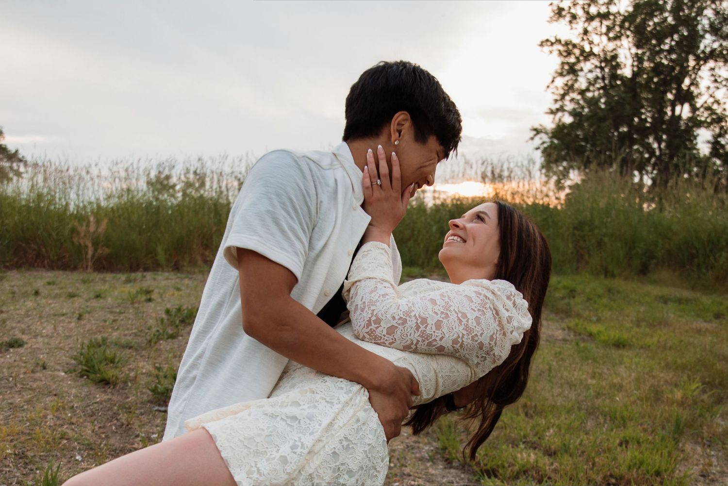 Romantic couple sharing a tender moment outdoors at sunset, woman leaning back while man holds her face gently.