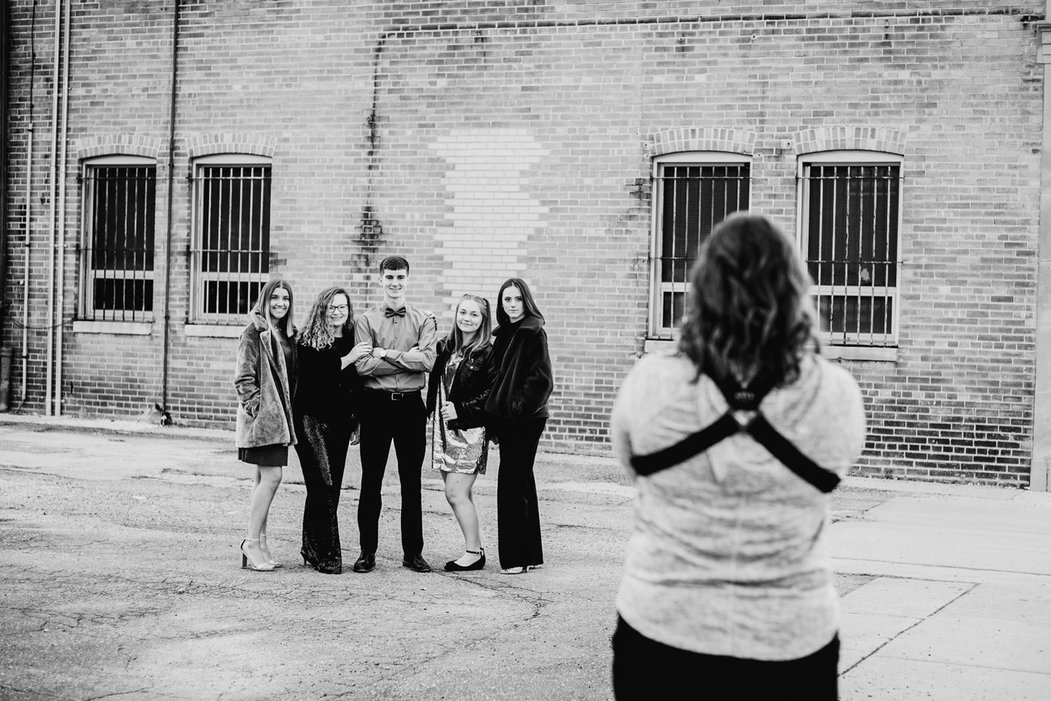 Photographer capturing group portrait of five people against brick wall, black and white.