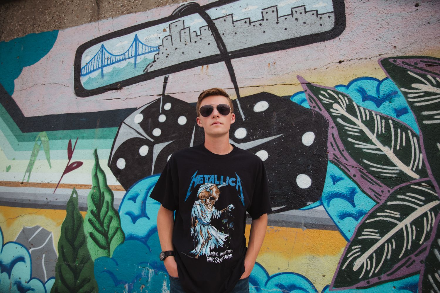 Teen boy in Metallica t-shirt and sunglasses posing in front of colorful graffiti wall.