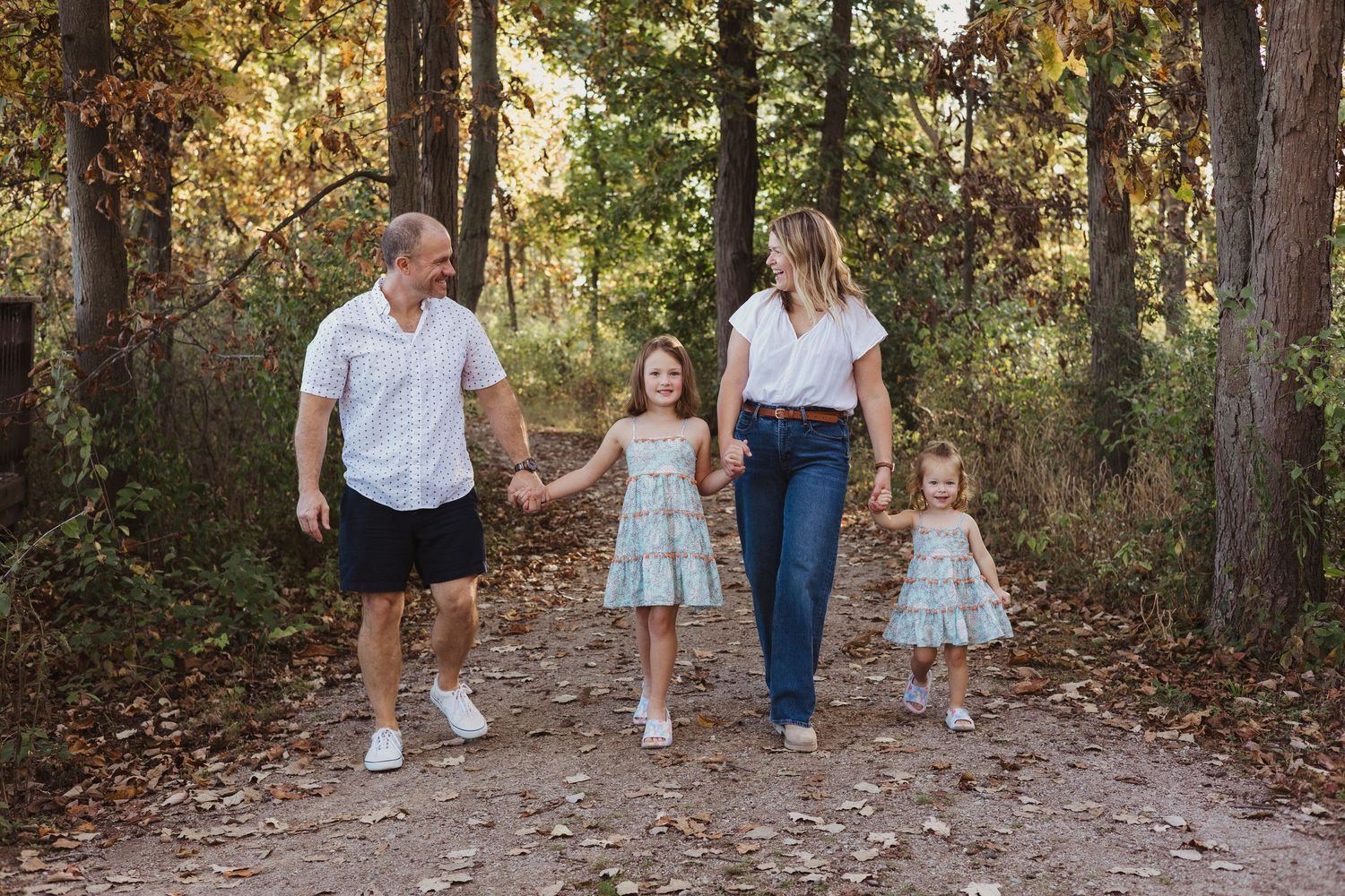 Family of four holding hands walking on a leaf covered forest path in autumn together.