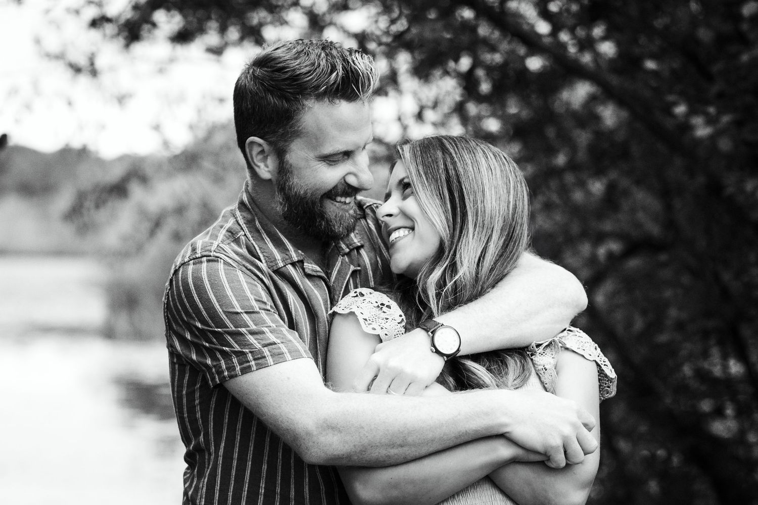 Couple sharing joyful embrace outdoors surrounded by trees in black and white.