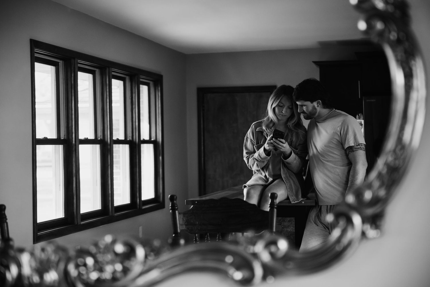 Black and white mirror reflection of a couple holding a newborn baby in a decorated room.