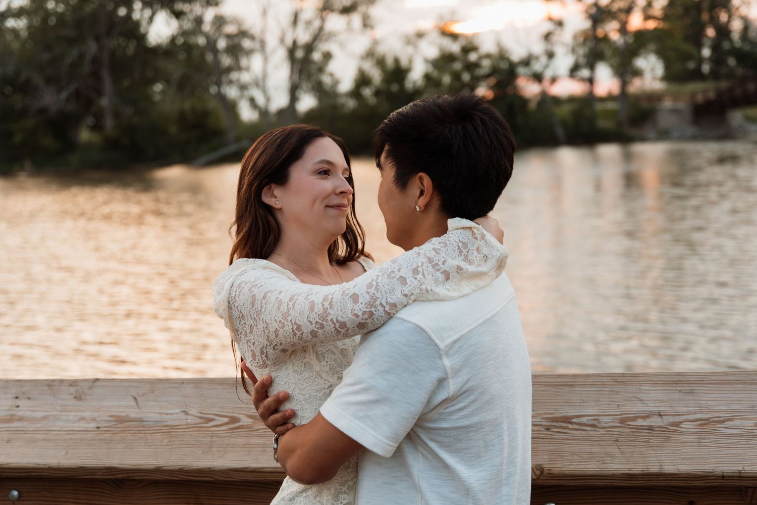 Romantic couple embracing and gazing at each other on a wooden dock at sunset.