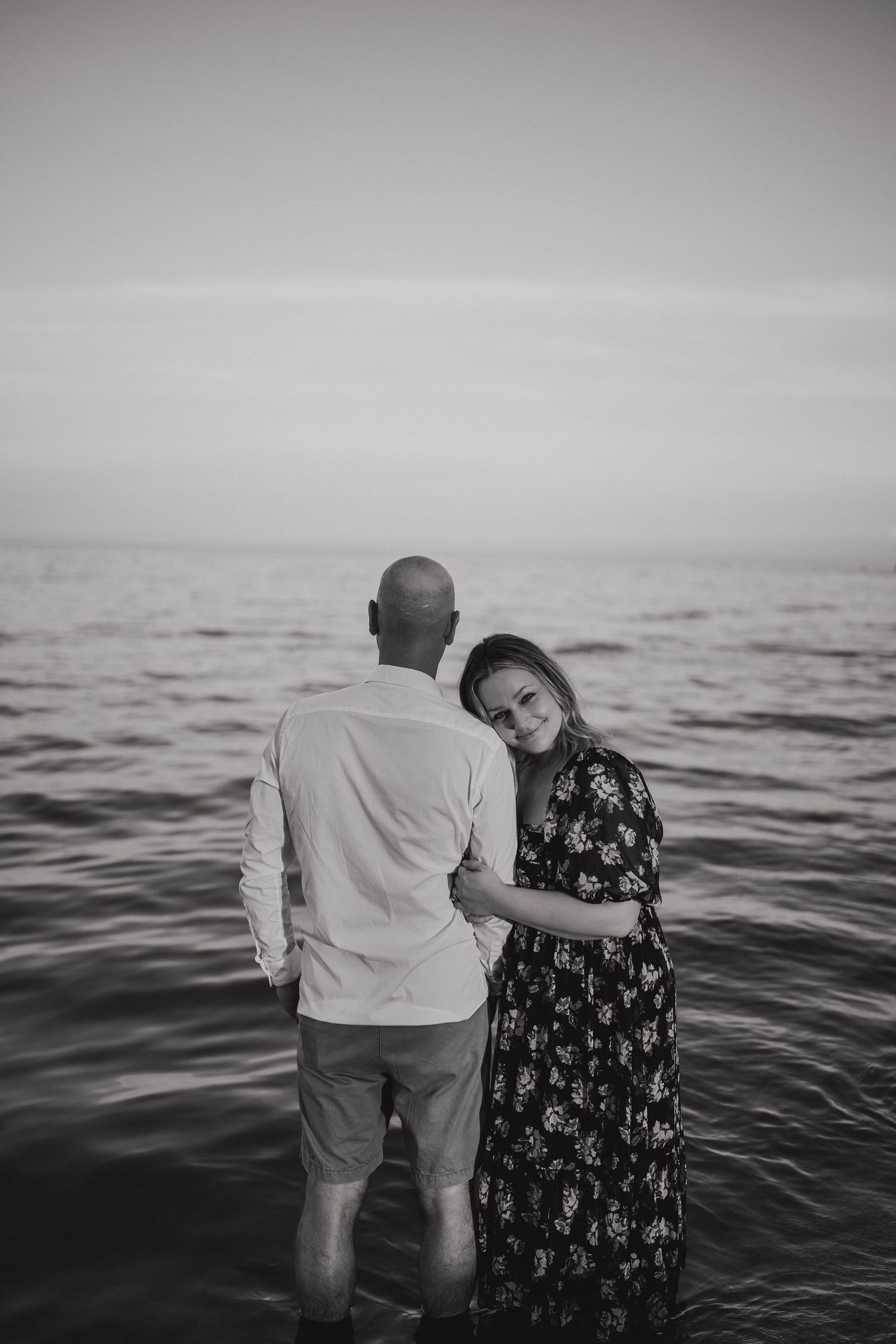 Black and white romantic couple photo standing in ocean water at dusk.