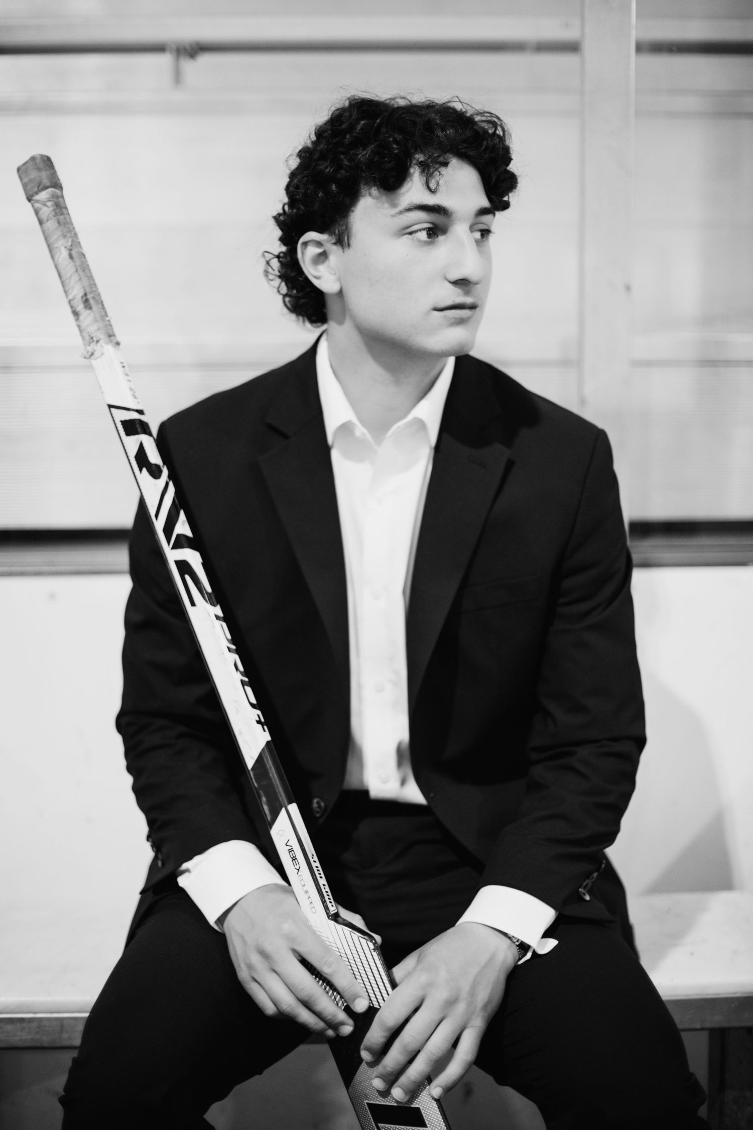 Young man in black suit holding a Bauer hockey stick, posed for a formal portrait in black and white.