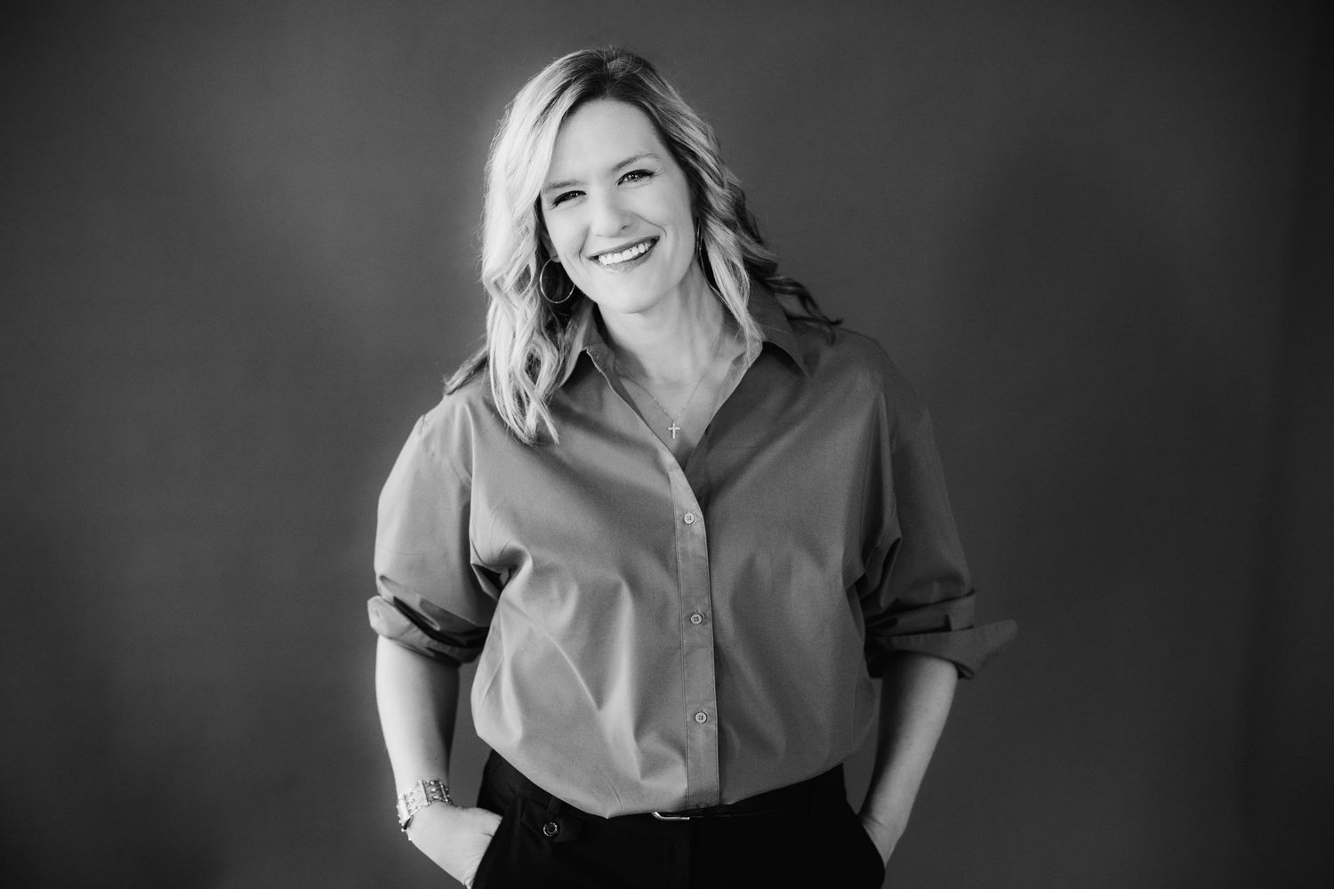 Black and white studio portrait of a smiling blonde woman in a button-up shirt.