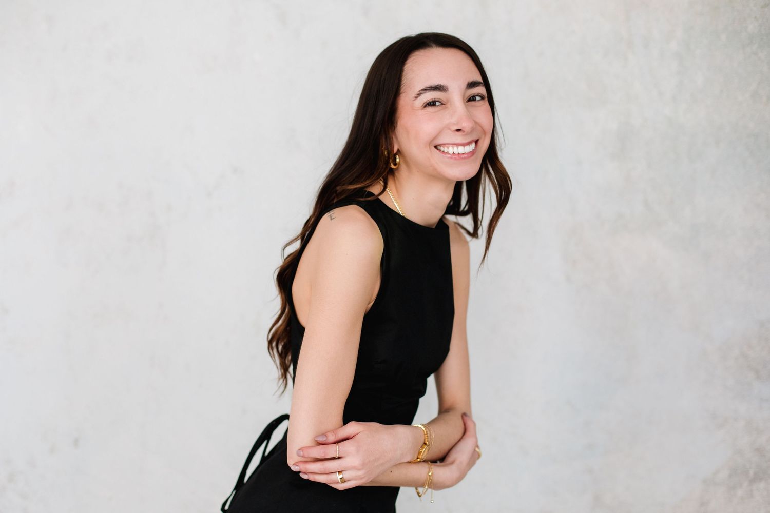 Smiling brunette woman in black dress laughing joyfully against gray background.