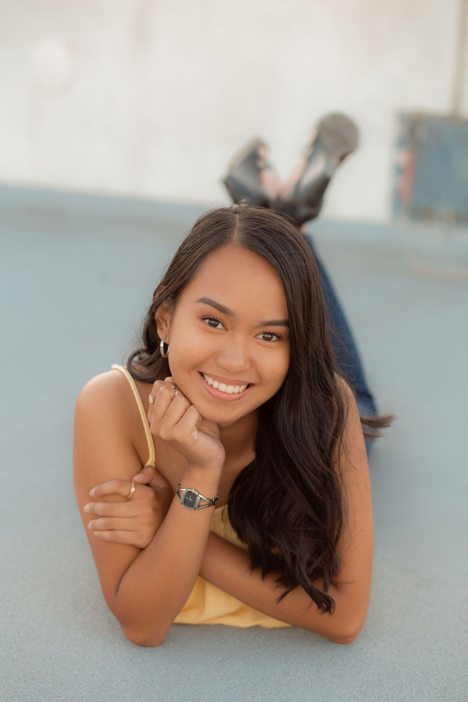 Smiling young woman in yellow top lies on ground with hand under chin in relaxed pose.