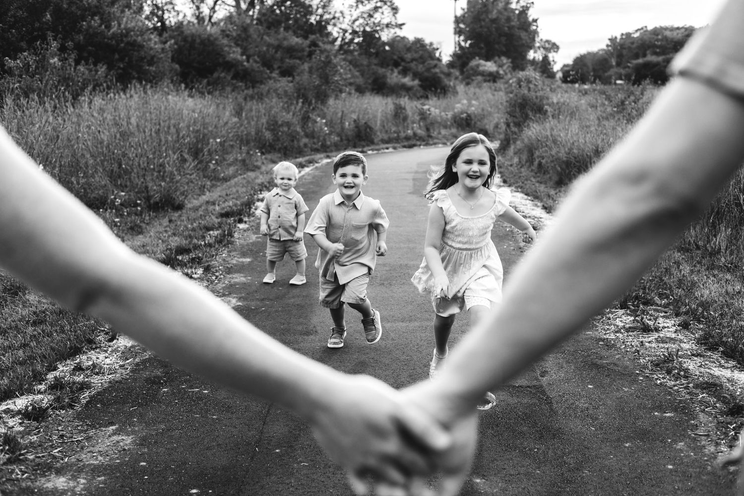 Black and white photo of three children joyfully running toward two adults holding hands on a rural path.