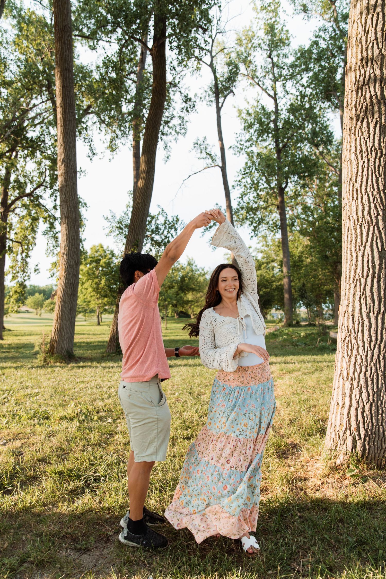 Couple dancing together in a sunny park, woman in floral skirt twirling as man lifts her hand.