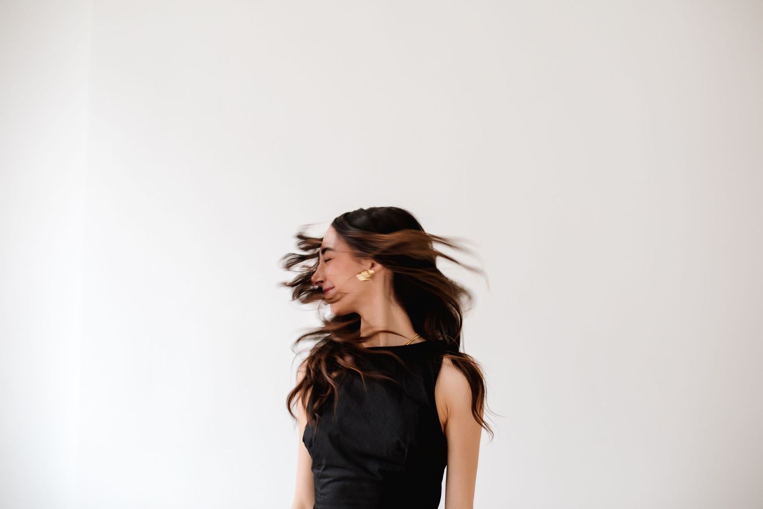 Young woman in black dress tossing long dark hair against white background.