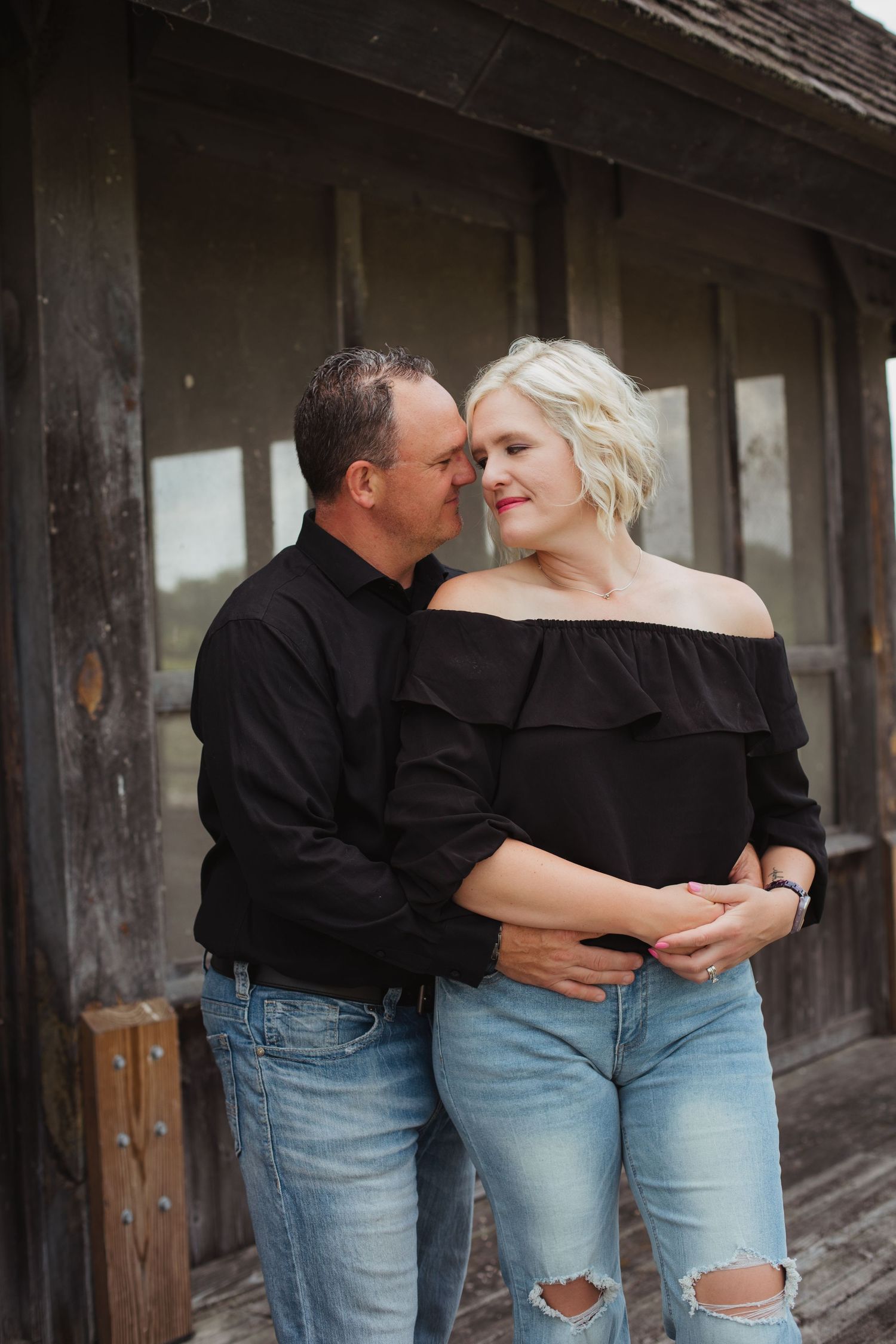 A loving couple shares a tender moment outside a rustic wooden building.