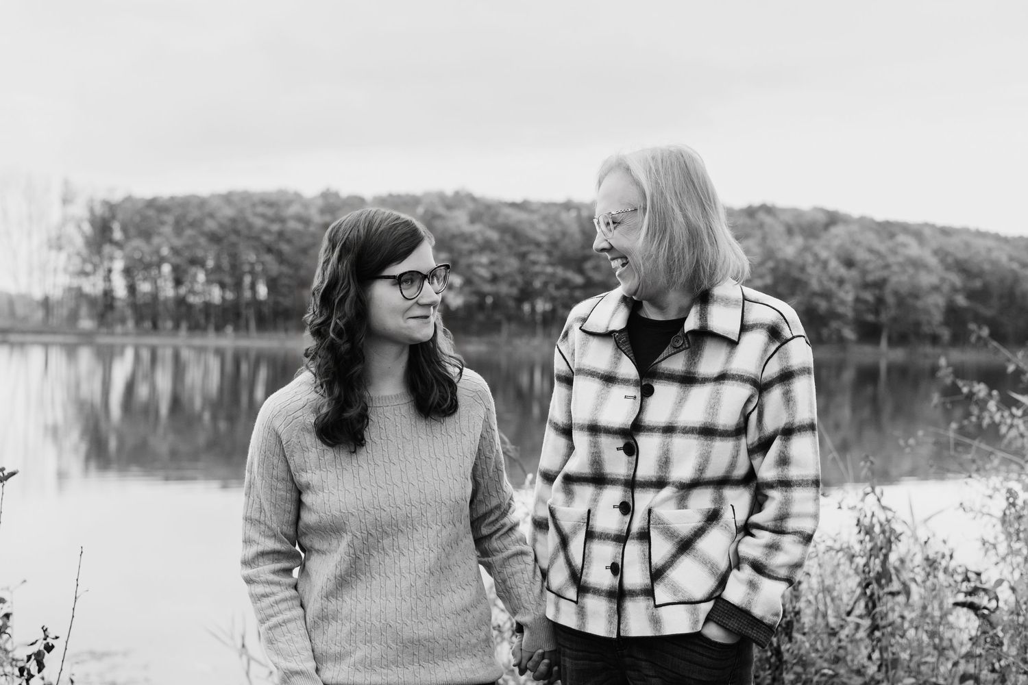 Black and white photo of two women holding hands by a lake in autumn.