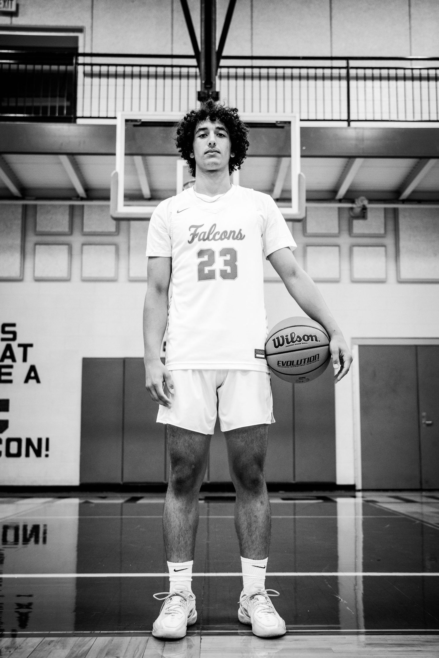 Black and white photo of a young male basketball player in Falcons #23 jersey holding a Wilson ball in a gym.