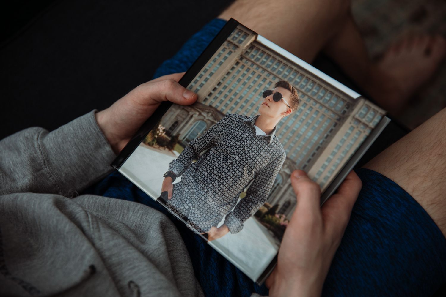 Person holding a printed photo of a man wearing sunglasses and a checkered shirt outdoors.