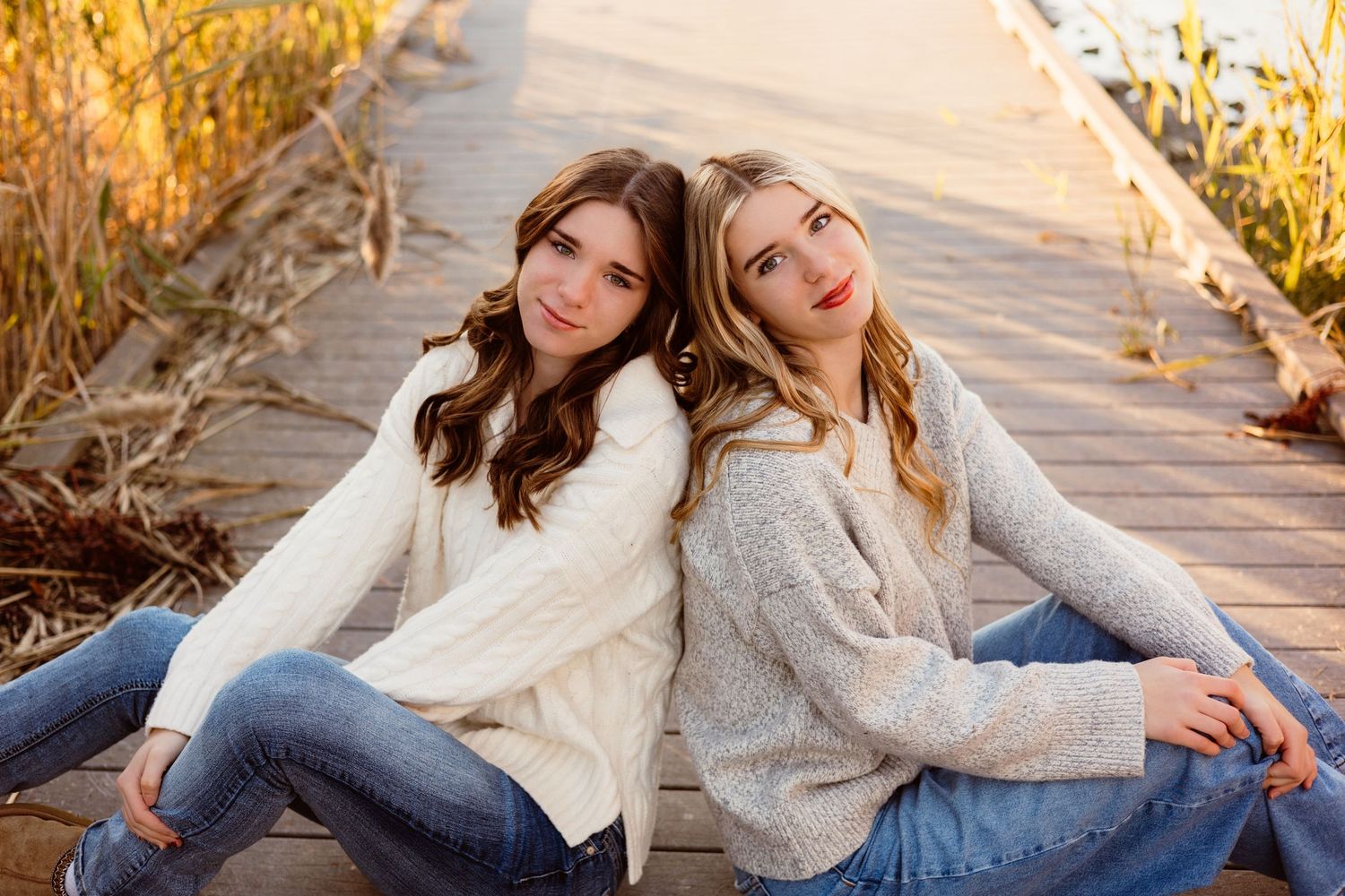 Two teenage girls sitting back to back on wooden boardwalk.