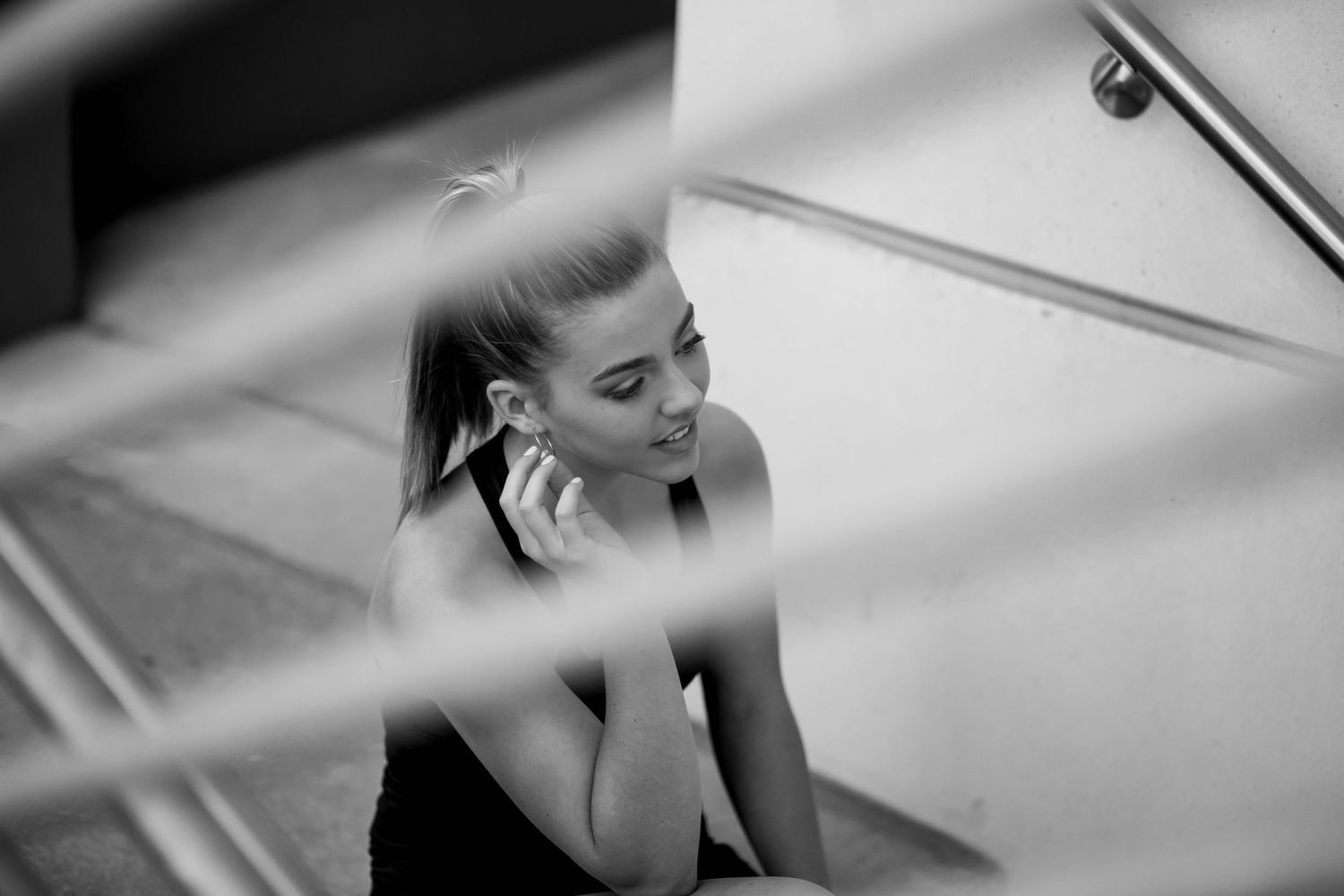 Black and white photo of a young woman sitting on stairs, talking on a phone, wearing a sleeveless top.