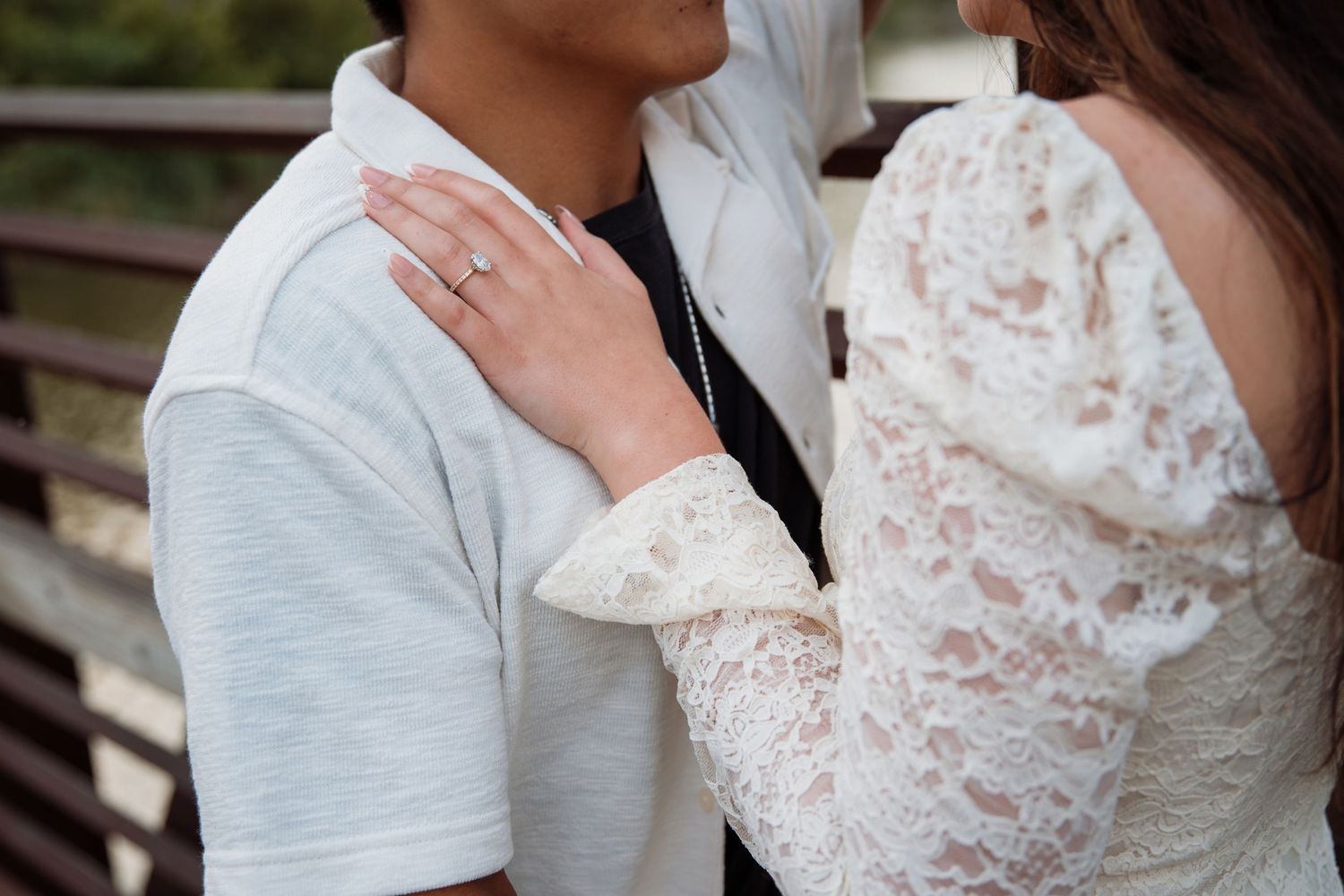 Close-up of womans hand with engagement ring resting on mans chest during outdoor photo session.