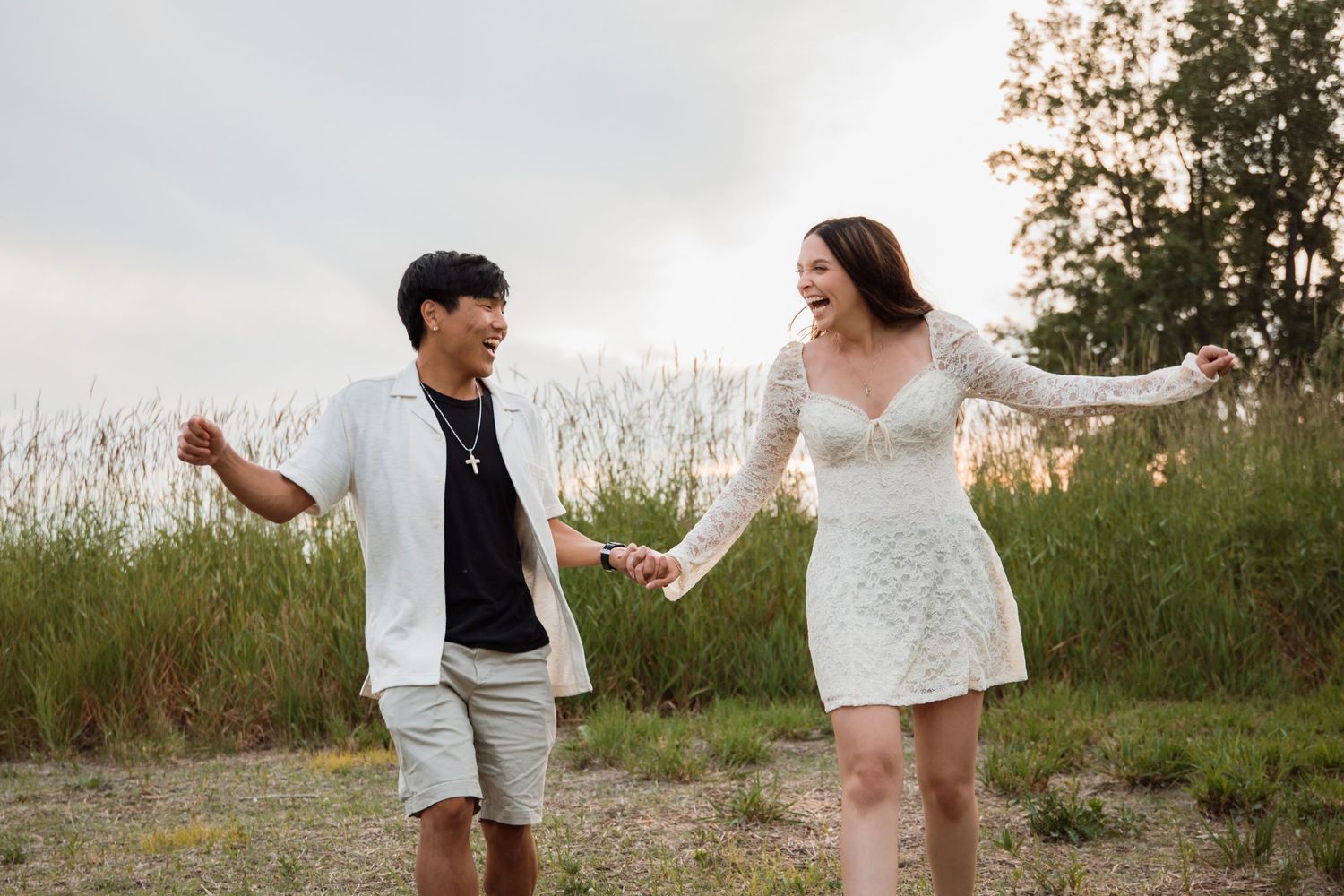 Joyful couple holding hands and laughing while walking through a sandy field at sunset.