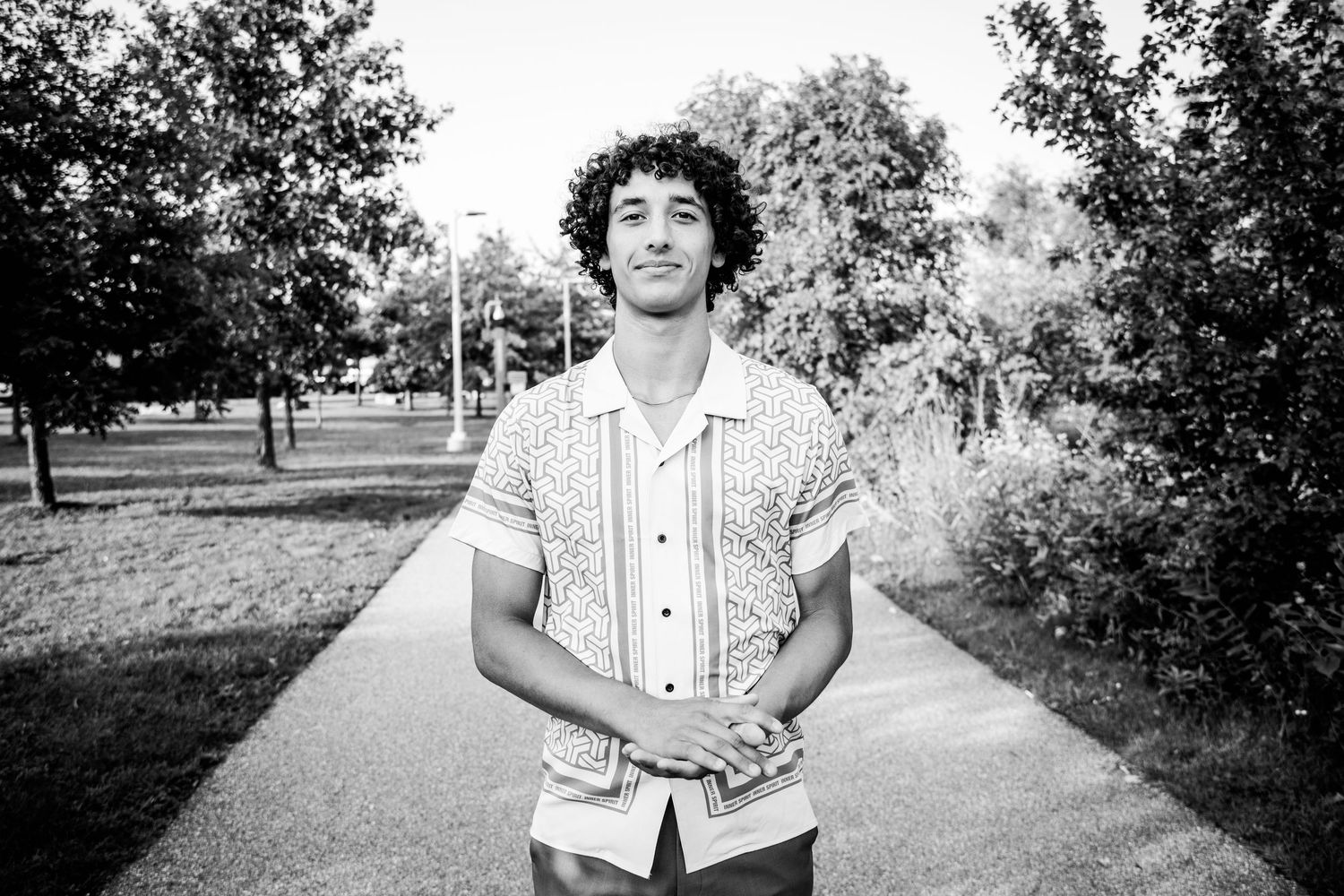 Young man with curly hair poses on a park path in black and white portrait photo.