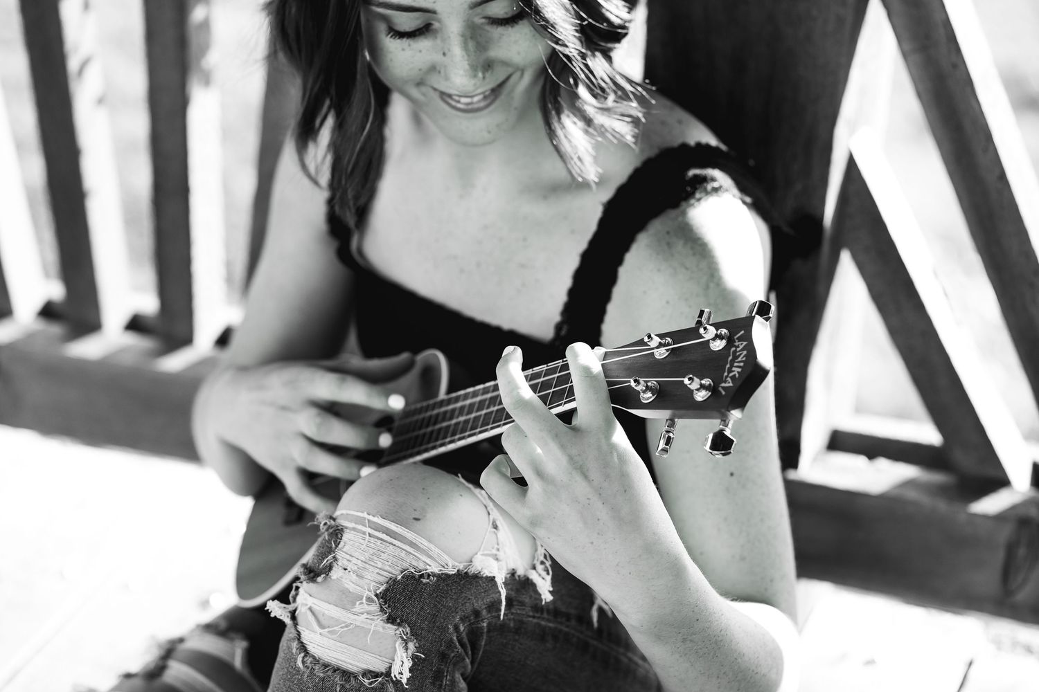 Young woman smiling while playing ukulele outdoors, black and white portrait photo.