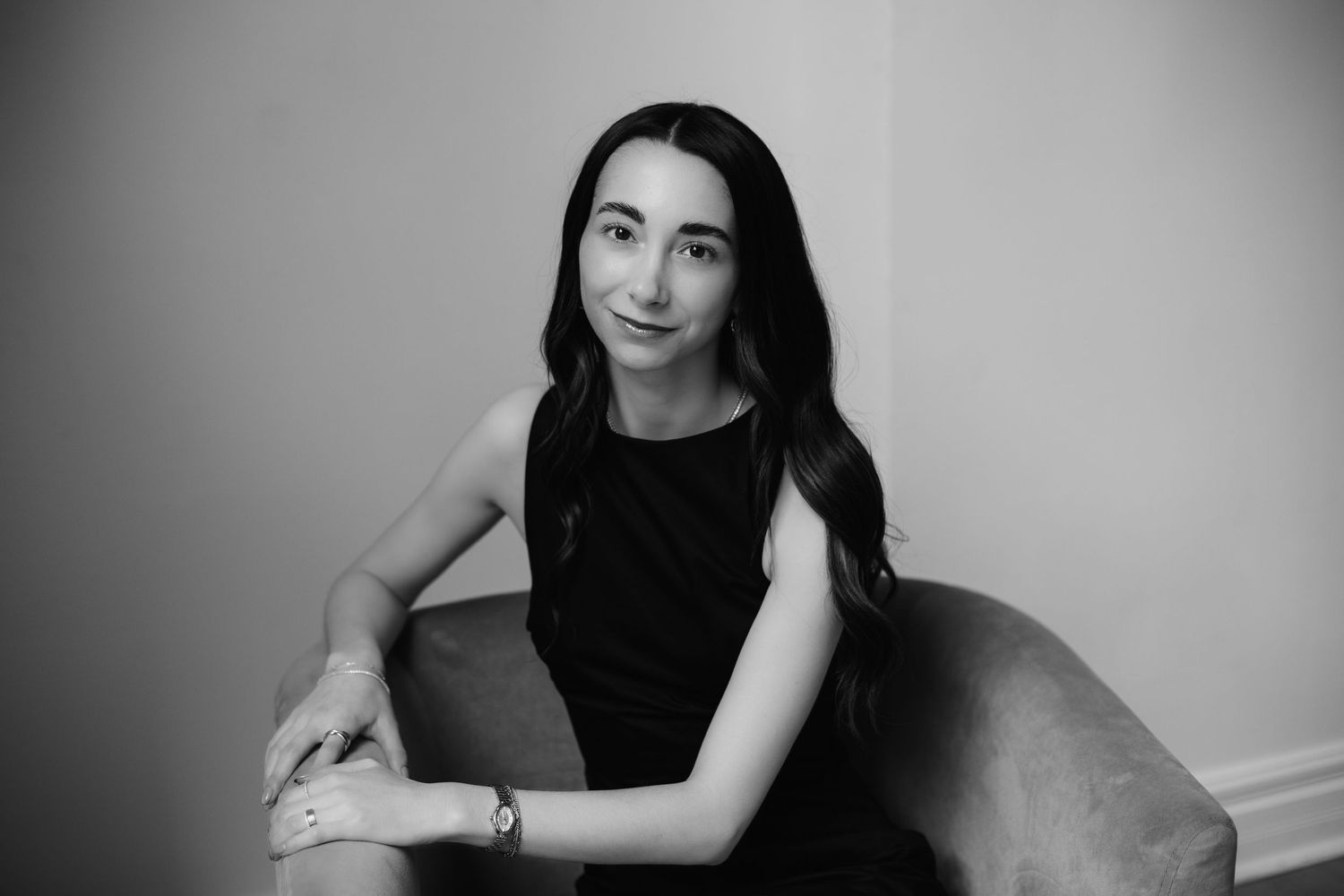 Black and white portrait of brunette woman seated in chair against neutral background.