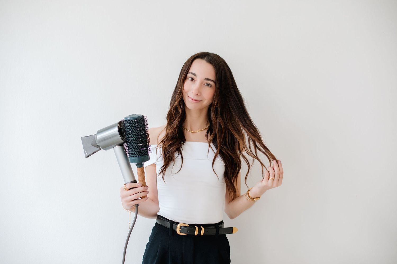 Brunette woman holding a hair dryer with diffuser attachment against a white background.