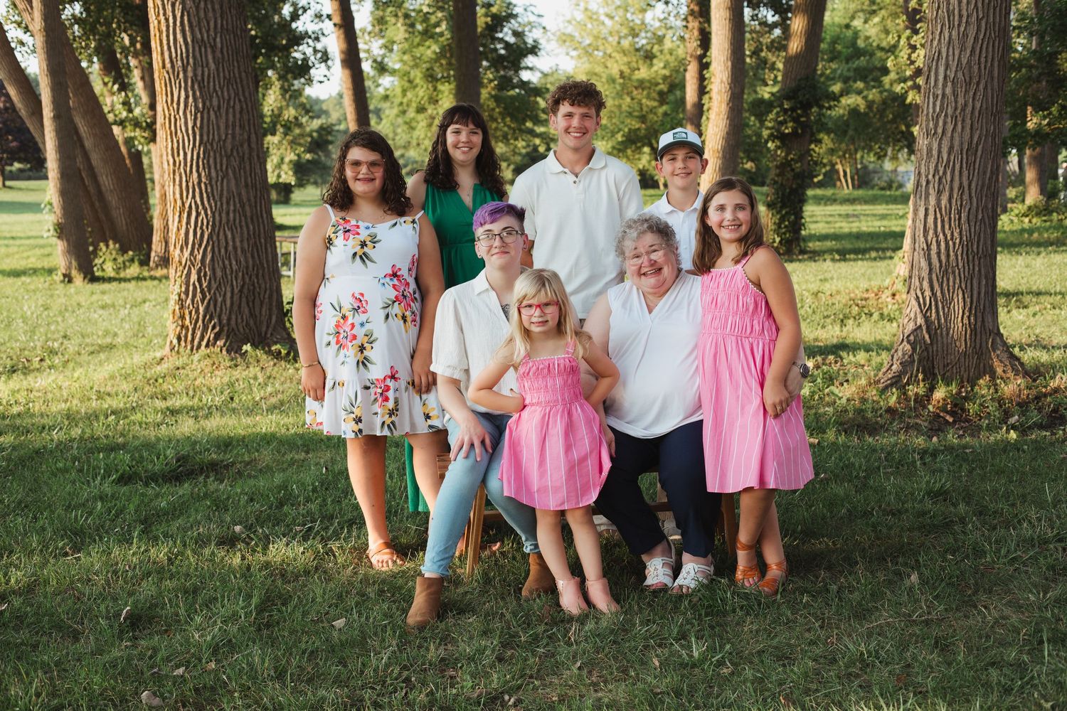 Extended family portrait session under tall trees in a park during summer.