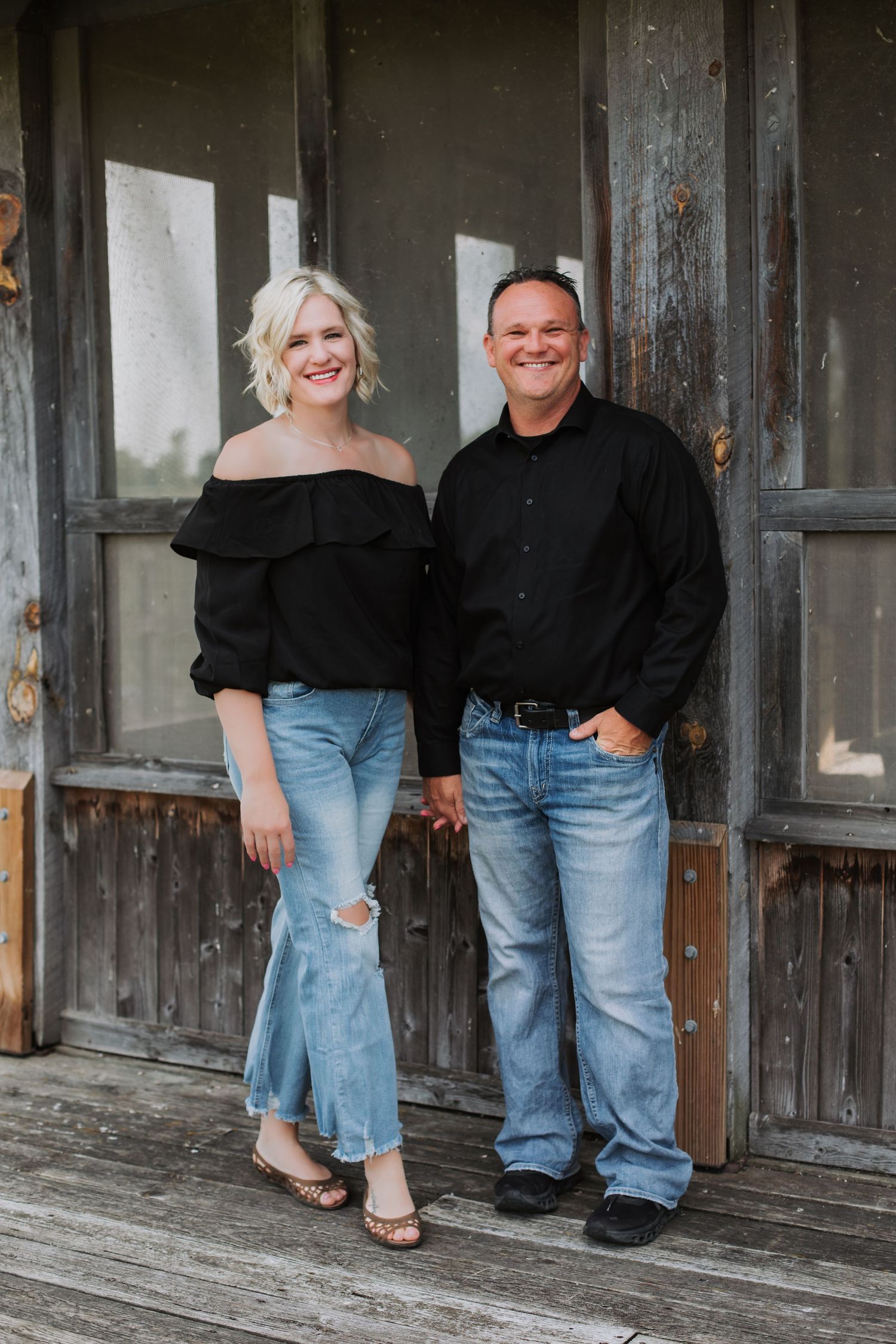 Couple in matching black tops and jeans posing in front of vintage wooden doors.