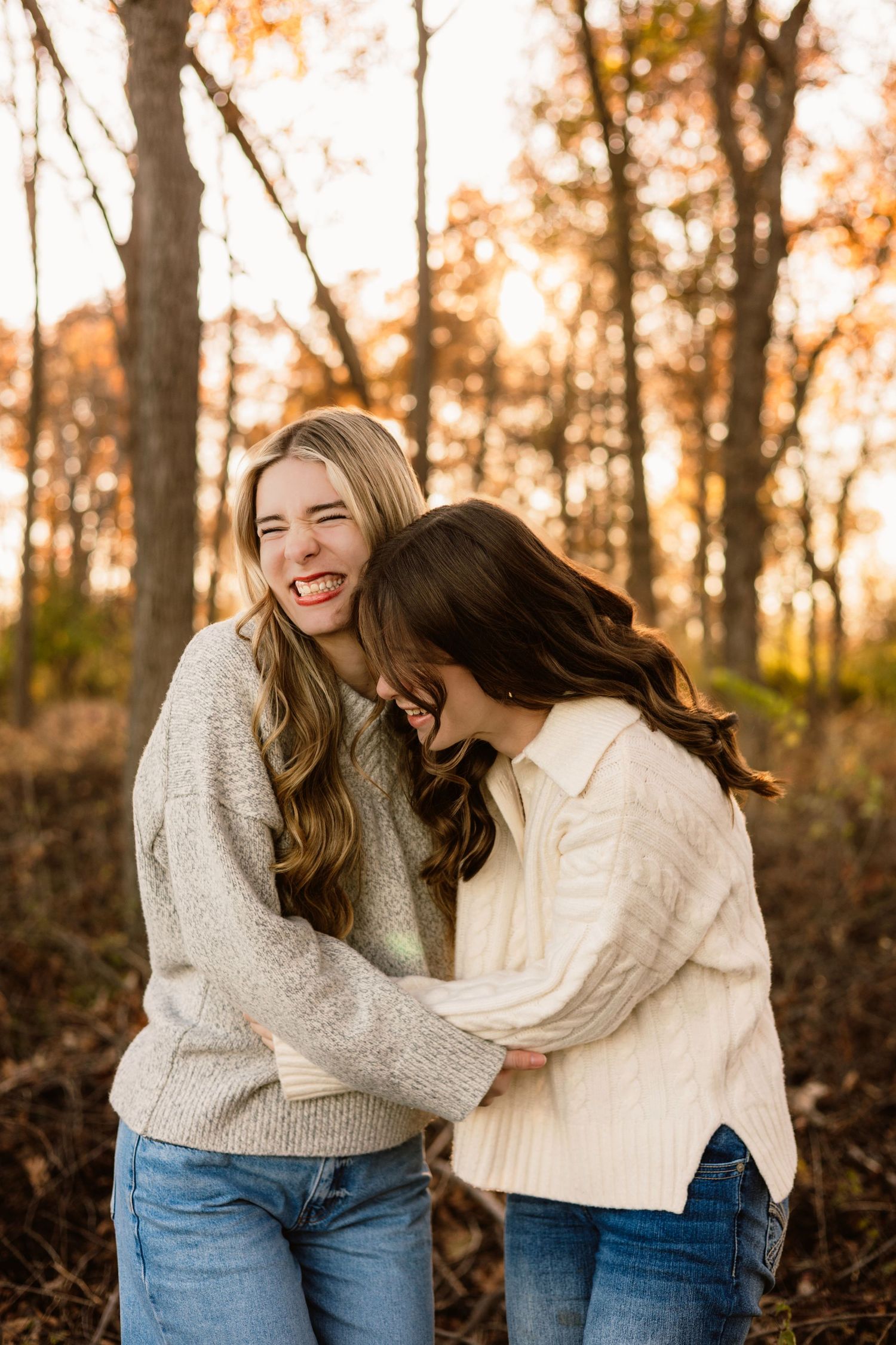 Two young women laughing and hugging in autumn forest.