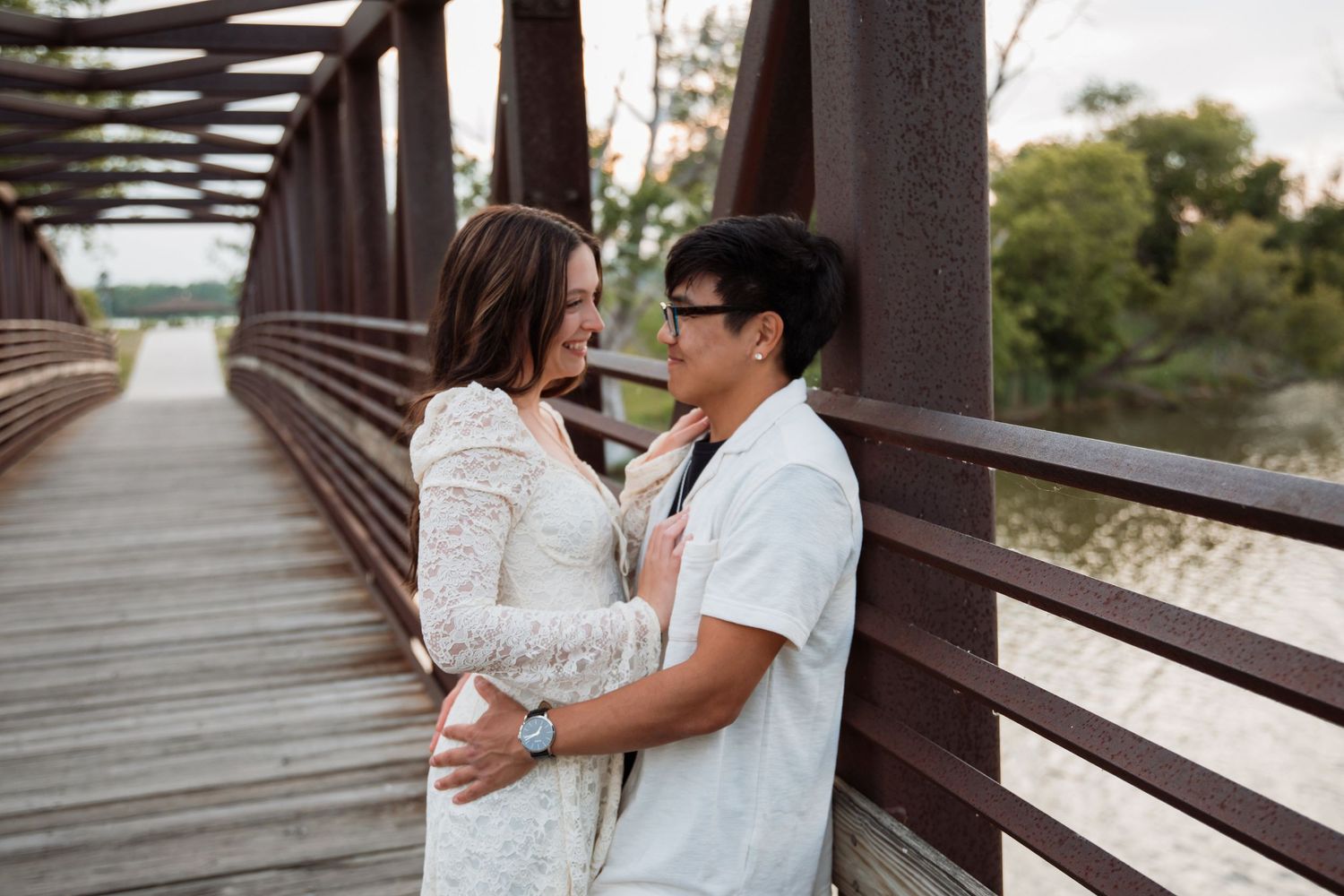 Couple sharing a romantic moment on a wooden bridge, smiling at each other in casual elegant attire.
