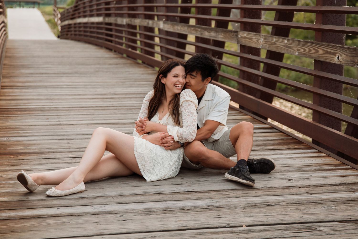 Romantic couple sitting together laughing on a wooden bridge boardwalk outdoors.
