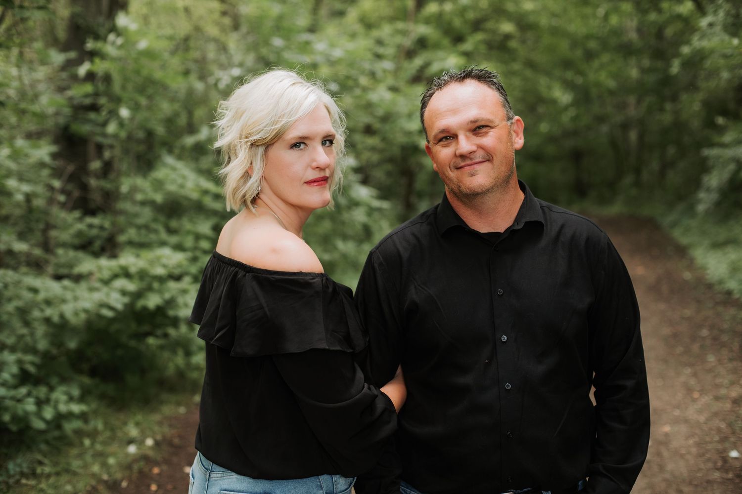 Couple in matching black outfits posing on a forest path.