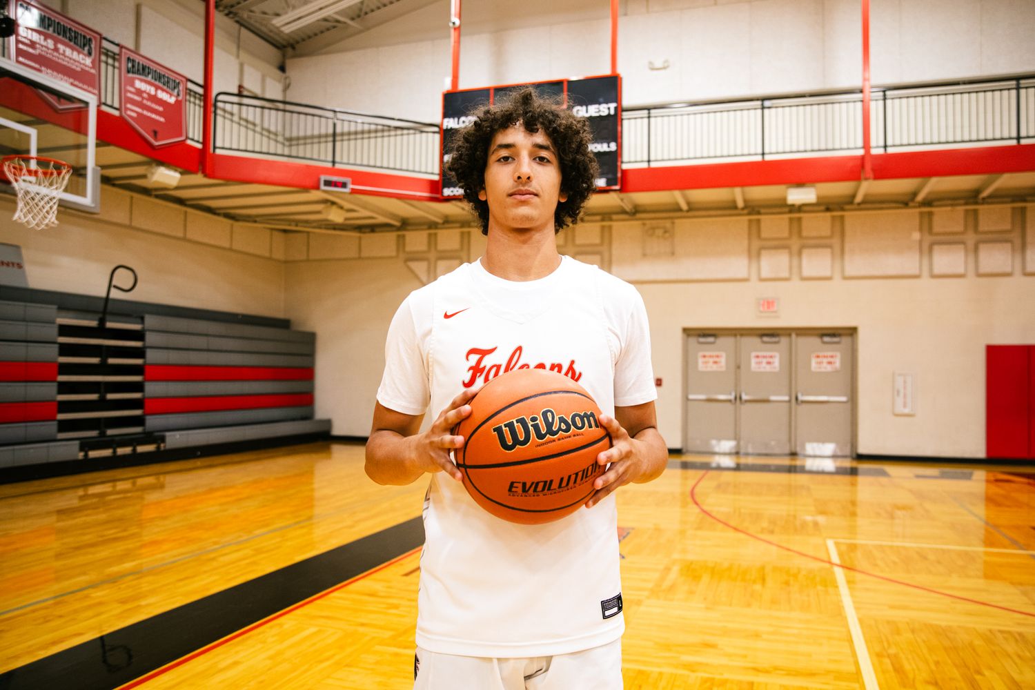 Young male basketball player in white Falcons jersey holding a Wilson basketball on an indoor court.