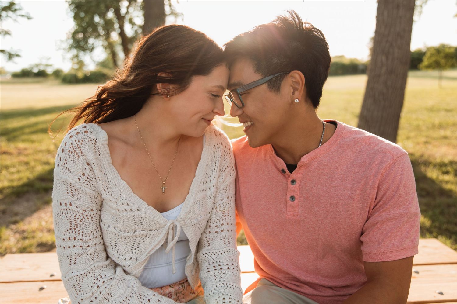 Couple sitting close together on a bench outdoors, foreheads nearly touching in a tender moment.