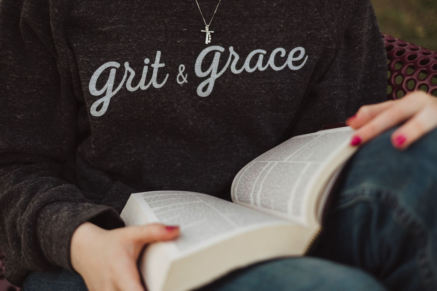Person wearing a Grit & Grace sweatshirt reading a book, showcasing faith-inspired Christian apparel.