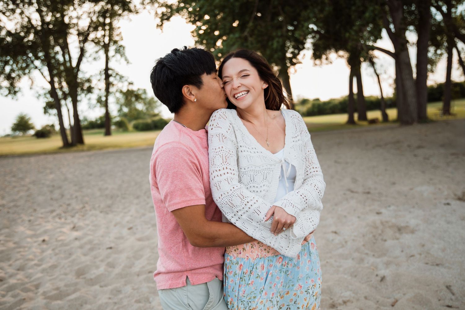 A young couple shares a tender moment on a sandy beach, with the man kissing the smiling woman's cheek.