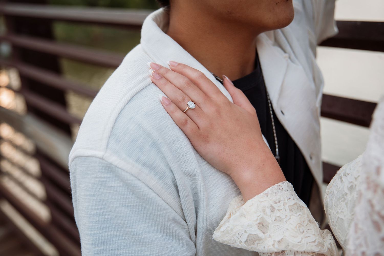 Close-up of a woman's hand with an engagement ring resting on a man's shoulder.