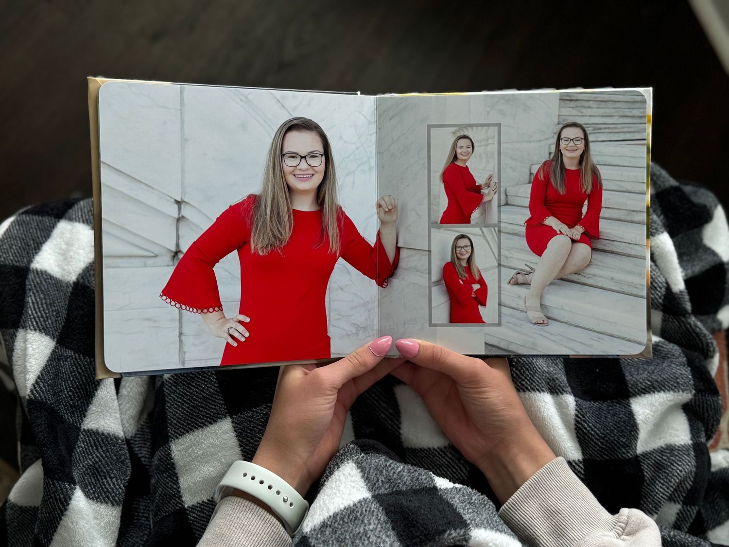 Hands holding open photo book featuring teenage girl in red dress senior portraits.