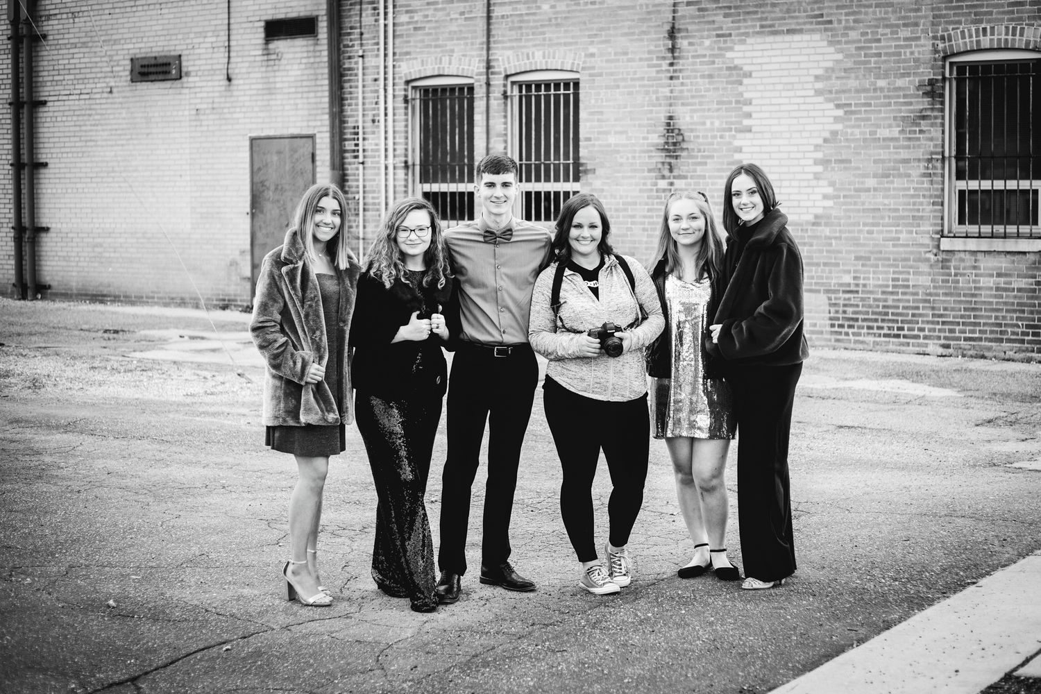 Black and white group photo of five young adults posing together on an urban street.