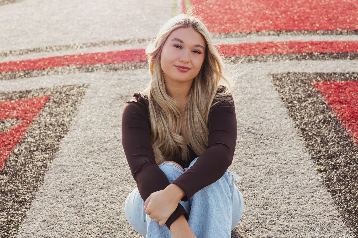Blonde teenage girl in black top and jeans sitting on decorative school field turf.