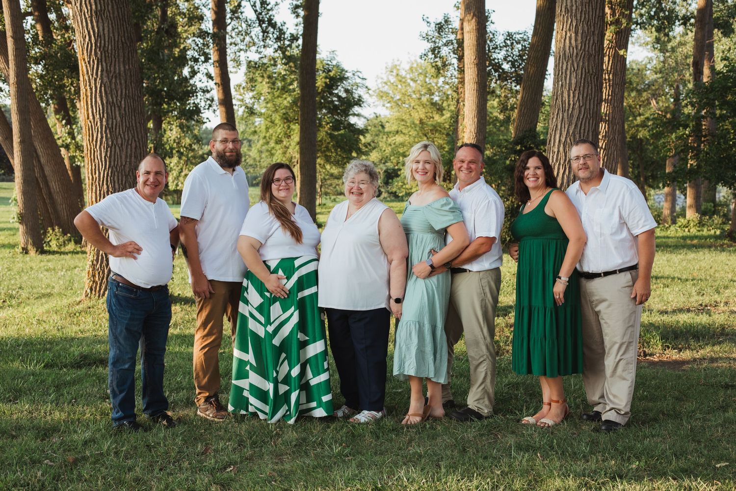 Large family group of eight adults posing together outdoors in a sunny park setting.