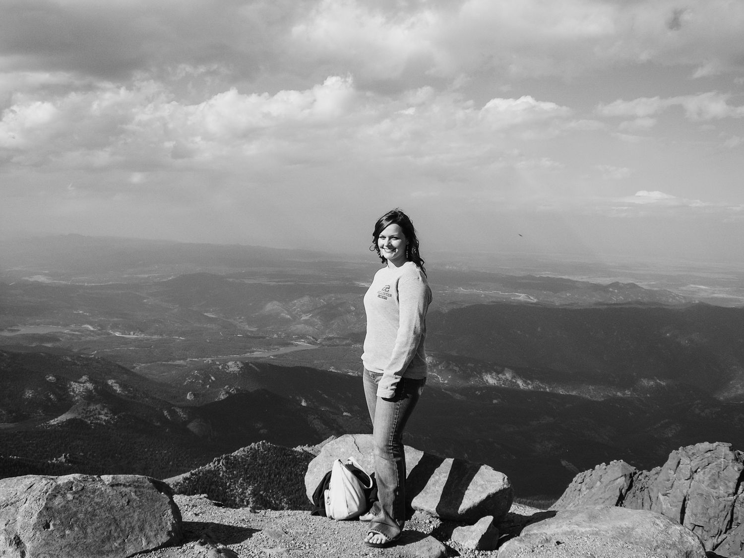 Woman standing on rocky mountain summit with panoramic valley views in black and white photography.
