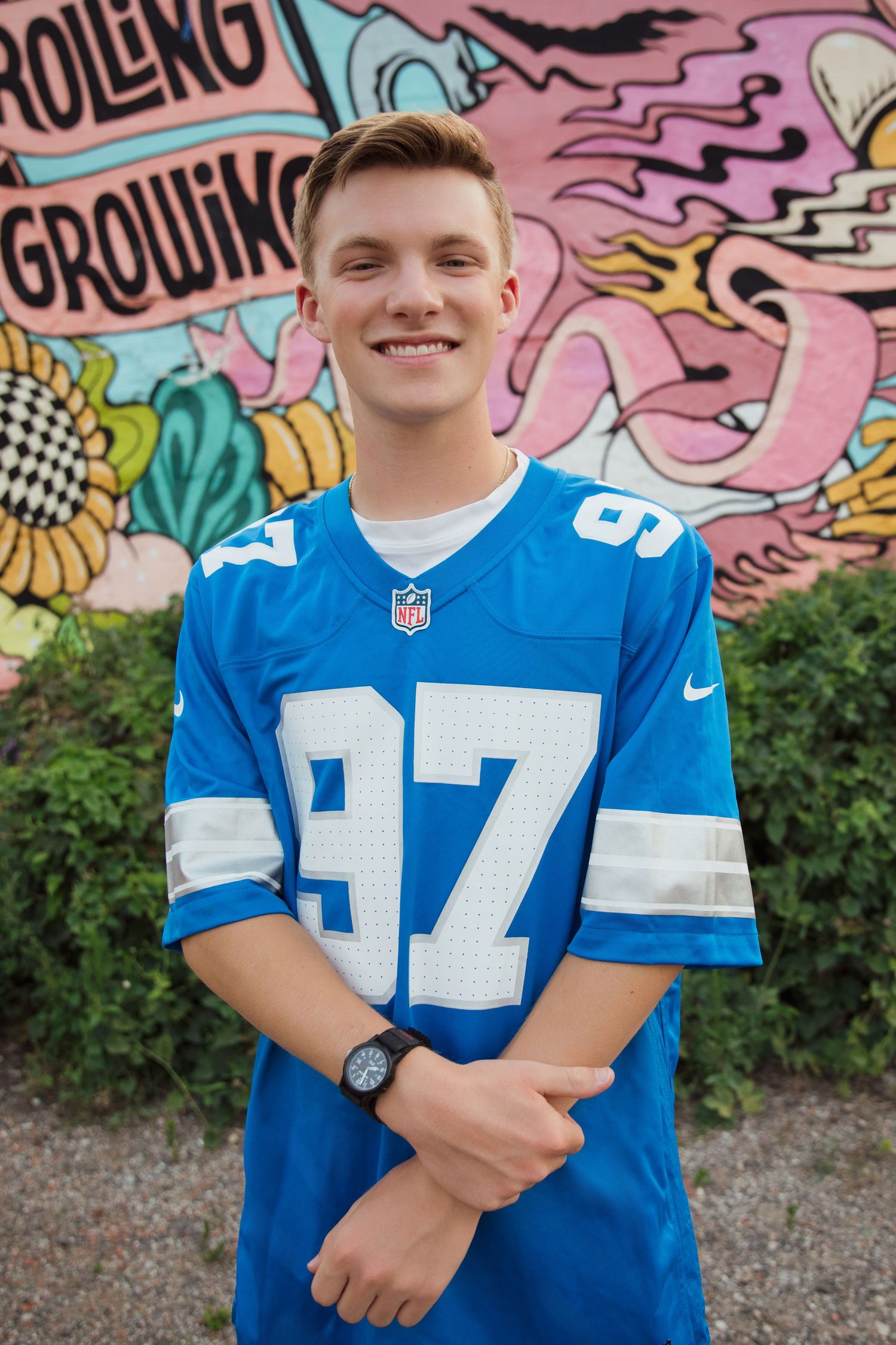Smiling teen in blue Lions NFL number 97 jersey posing before colorful street mural.