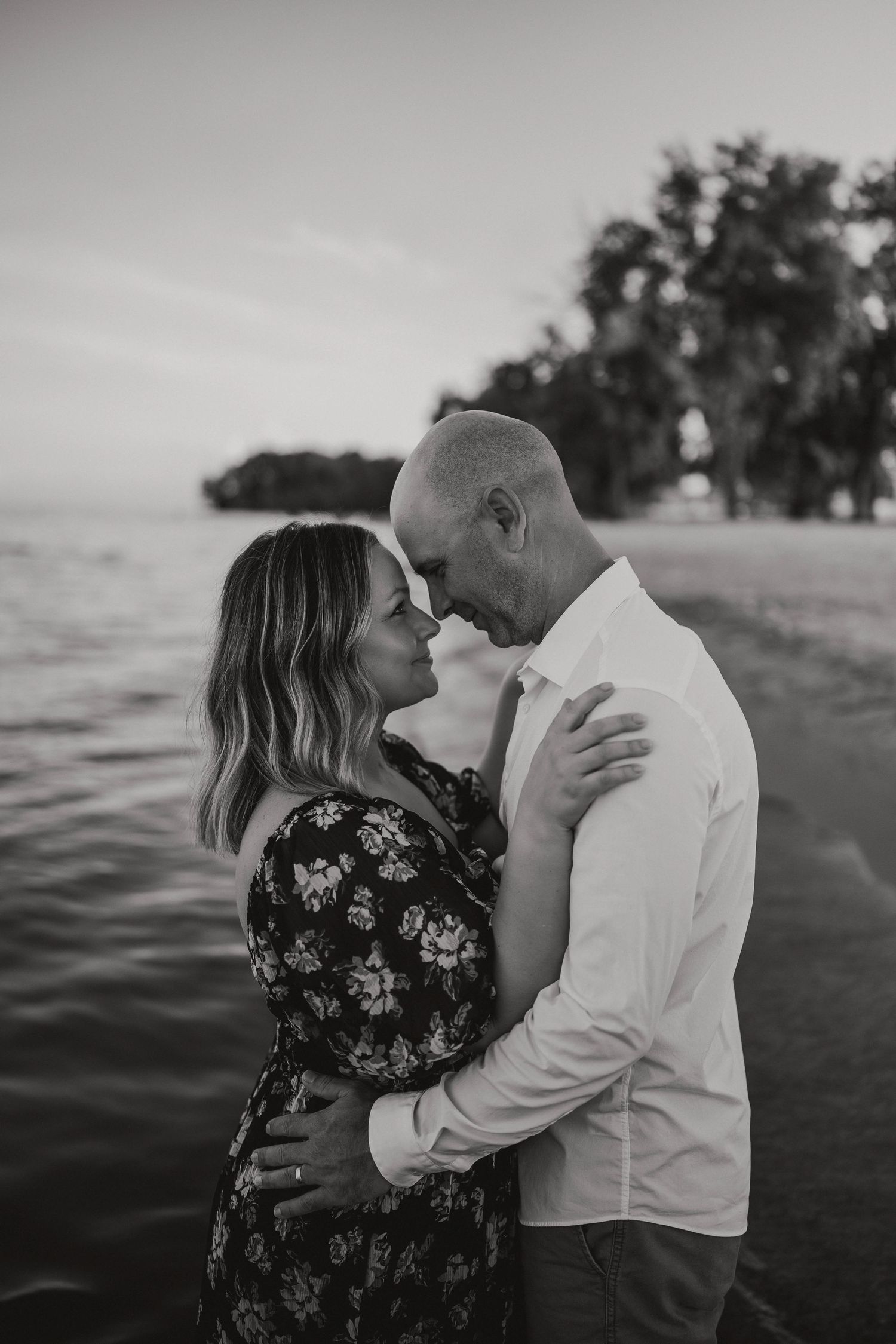 Black and white romantic couple embracing near a serene beach at sunset.