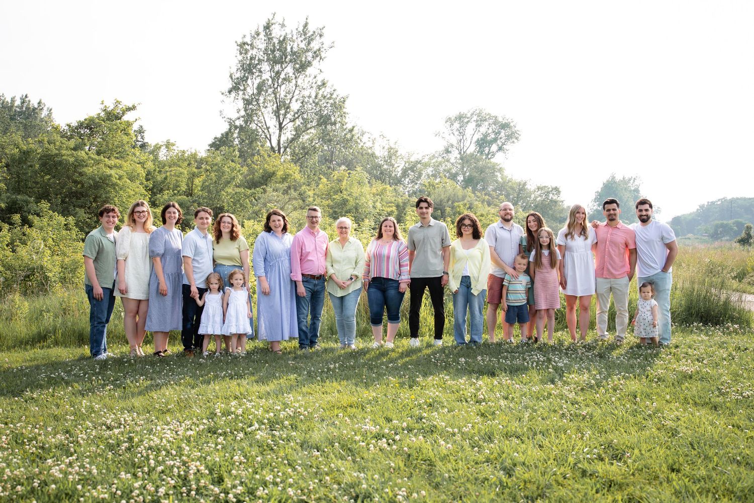 Large extended family group portrait standing together in a sunny green meadow.