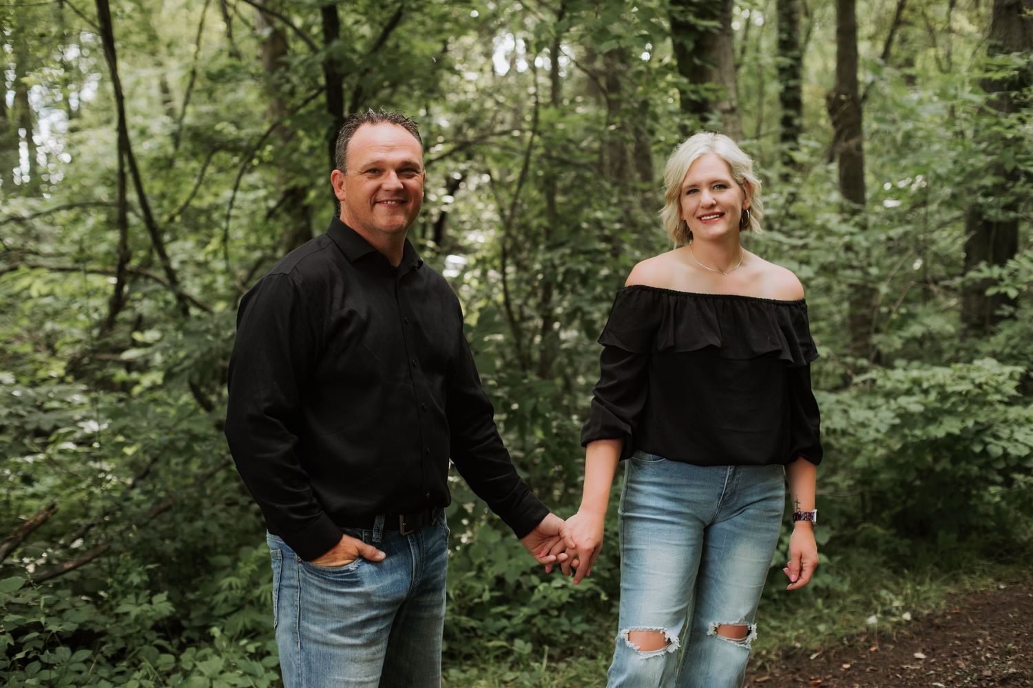 Couple holding hands and walking along a wooded forest trail.