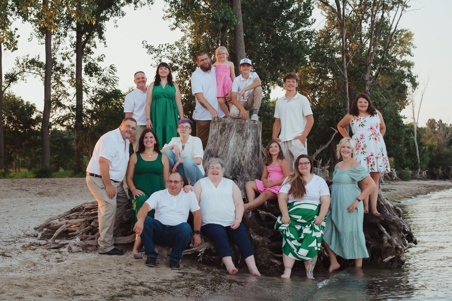 Large extended family posing together on a driftwood log near a scenic lakeside beach.